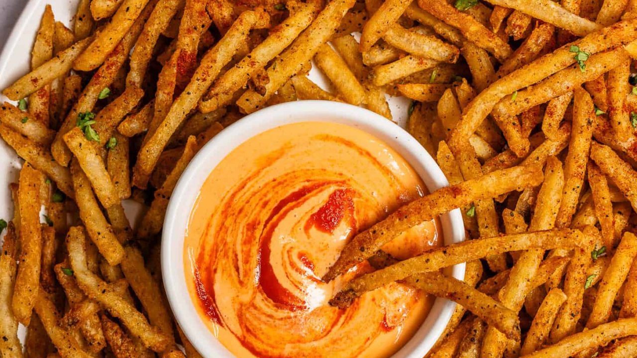 Fries being dipped into Sriracha Mayo